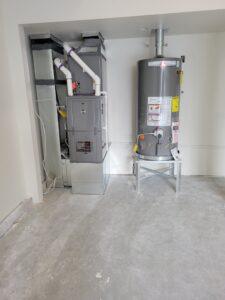 Rheem water heater and high-efficiency furnace installed side by side in a residential utility space, featuring neatly connected piping and ductwork.