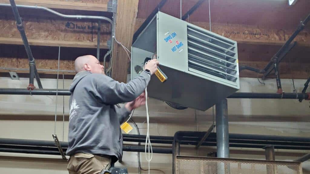 Technician installing a ceiling-mounted heater in a commercial space for efficient heating.