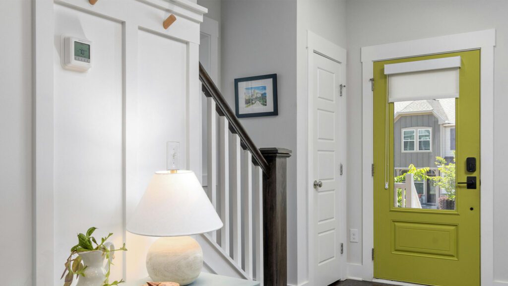 Bright and modern home entryway featuring a green front door, a staircase, and a wall-mounted smart thermostat set to 70°F for optimal comfort